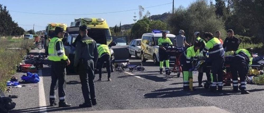 Rettungskräfte und Polizisten stehen am Unfallort, an dem ein Auto in eine Gruppe von 15 Radfahrern aus Deutschland gefahren ist. 