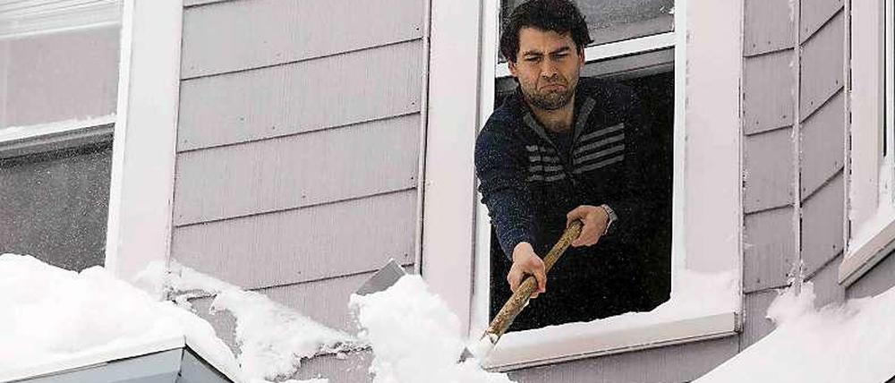 Ein Mann in Boston schaufelt Schnee von seinem Vordach. Er hat sich mit den Schneebergen noch nicht so angefreundet, wie es scheint. Warum springt er nicht aus dem Fenster, wie es viele seiner Nachbarn unternehmen?