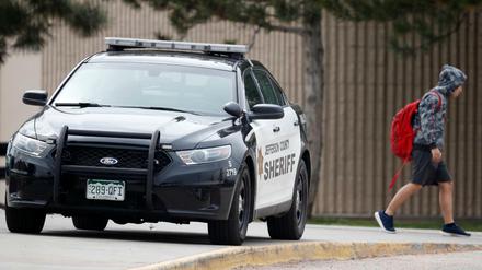 Ein Polizeiauto steht vor der Columbine High School, während Schüler diese verlassen.