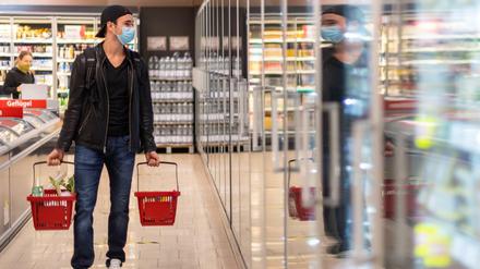 Ein Kunde geht in einem Supermarkt einkaufen und trägt dabei eine Maske.