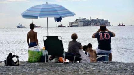 Vom Strand aus beobachten Urlauber, wie die Costa Concordia in Genua ankommt.