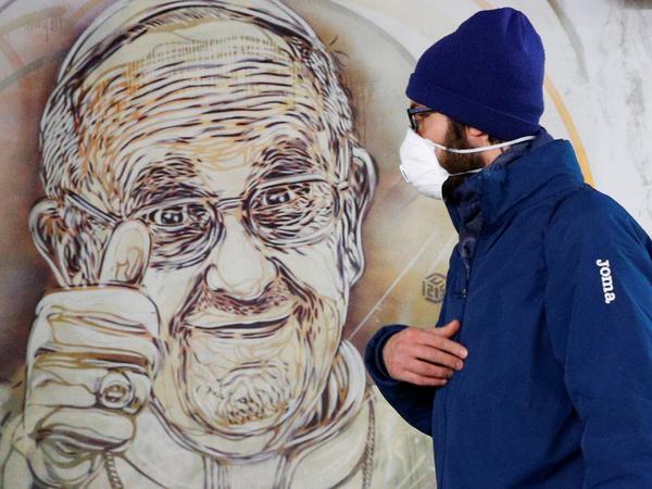 Ein Mann geht in Rom an einem Bild des Papstes vorbei.