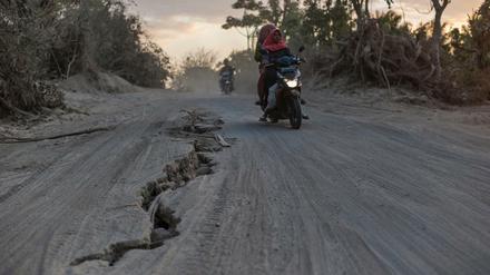 Eine Frau fährt mit ihrem Roller auf einer Straße, die vom Erdbeben aufgerissen wurde. 