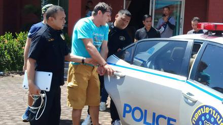 Francesco G. aus Italien, der von thailändischen Polizisten zu einem Polizeiauto geführt wird.
