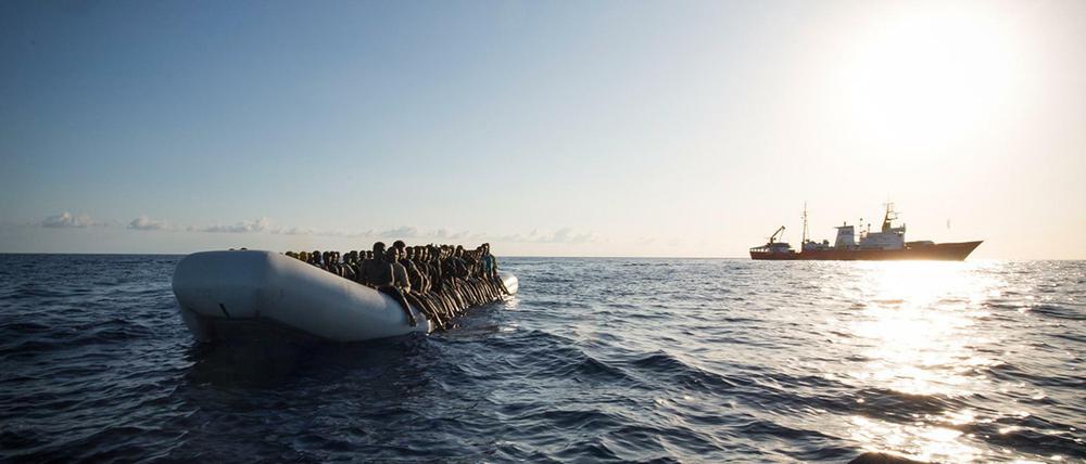 Ein Flüchtlingsboot auf dem Mittelmeer und im Hintergrund ein Schiff der Hilfsorganisation SOS Mediterranee.