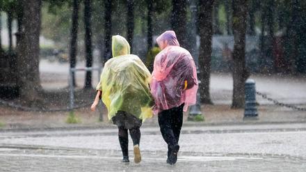 Passanten mit Plastik-Regenschutz gehen nahe des Brandenburger Tors durch den Regen. 