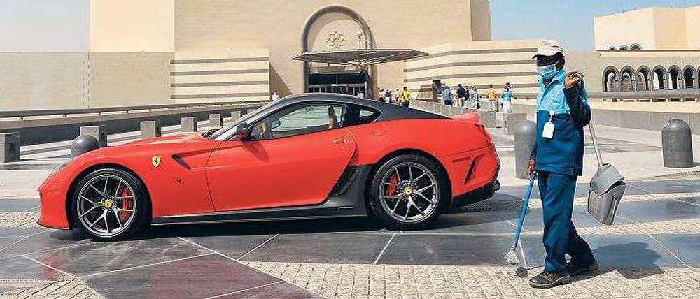 Reichtum und Ausbeutung. Ein ausländischer Arbeiter steht vor einem Ferrari in Katar. 