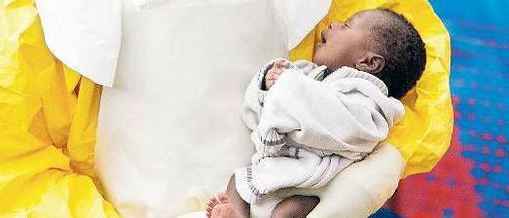Ein Arzt in Guinea hält ein Baby im Arm, das infiziert sein könnte. 