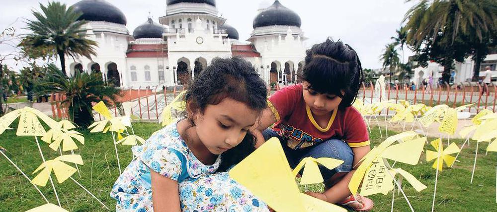 Blumen des Mitgefühls. Kinder stecken Papierblumen vor der Großen Baiturrahman-Moschee in Banda Aceh in Indonesien zum Gedenken in die Erde. Die Grüße kommen aus Japan, mehr als 40 000 Japaner haben eine handgeschriebene Nachricht mitgeschickt.