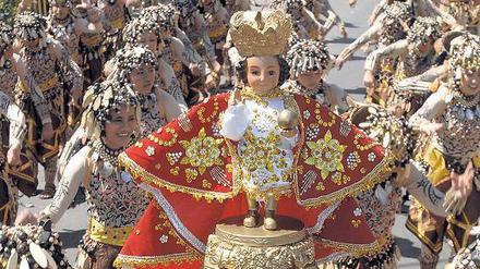 Katholische Zeremonie auf den Philippinen. Viele Teilnehmer halten Santo-Niño-Figuren aus Elfenbein in die Höhe. Sie geben viel Geld dafür aus, um Gott zu huldigen. 