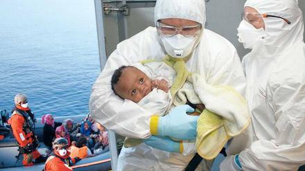 Ein Helfer nimmt im Mittelmeer auf der Fregatte „Hessen“ ein gerettetes Baby in Empfang. 
