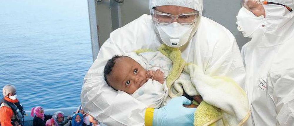 Ein Helfer nimmt im Mittelmeer auf der Fregatte „Hessen“ ein gerettetes Baby in Empfang. 