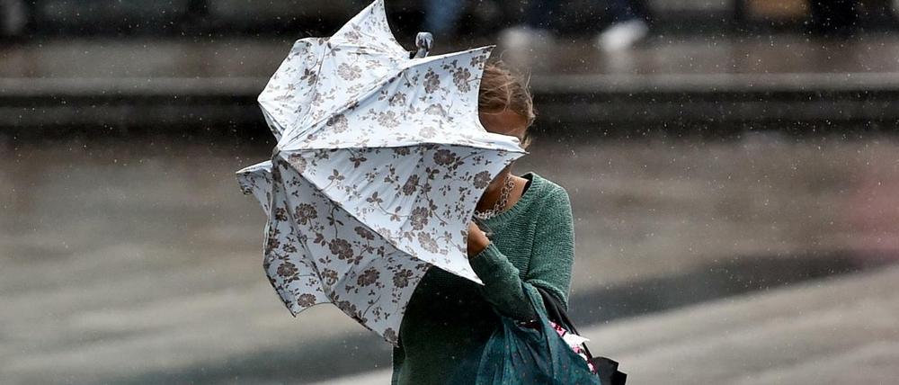 Eine junge Frauen kämpft in Berlin bei Starkwind mit einem Regenschirm. (Symbolbild)