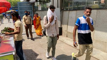 Ein Mann bedeckt sich mit einem Stück Stoff, um sich vor der Hitze zu schützen, während er vor einer U-Bahn-Station in Neu Delhi entlang geht.