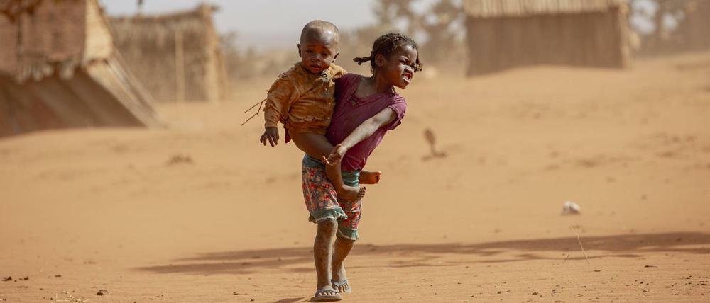 Ein Mädchen trägt ein kleines Kind im Süden Madagaskars durch den Staub.