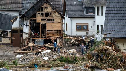 Anwohner gehen in dem Ort im Kreis Ahrweiler nach dem Unwetter mit Hochwasser durch den Schutt an einem beschädigten Gebäude vorbei.