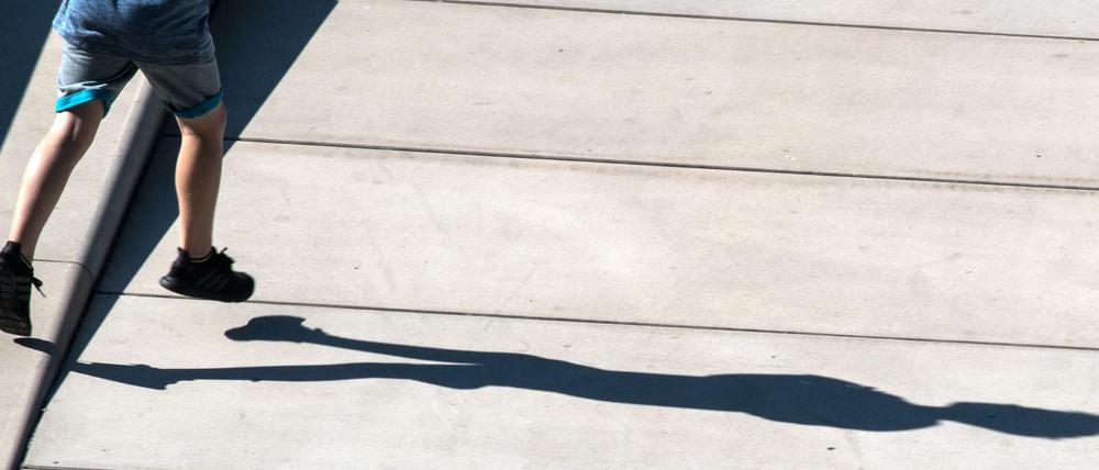 Ein Junge wirft beim Laufen einen langen Schatten auf des Pflaster. (Symbolbild)