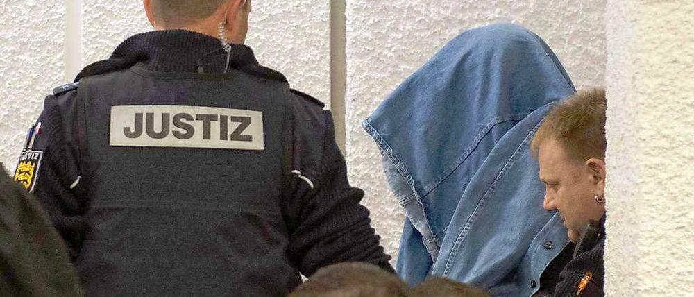 Der Angeklagte im Koffermord-Prozess, Günter H., der Handschließen und eine Jacke über dem Kopf trägt, wird am Montag in Stuttgart von einem Justizbeamten in einen Gerichtssaal im Landgericht geführt.