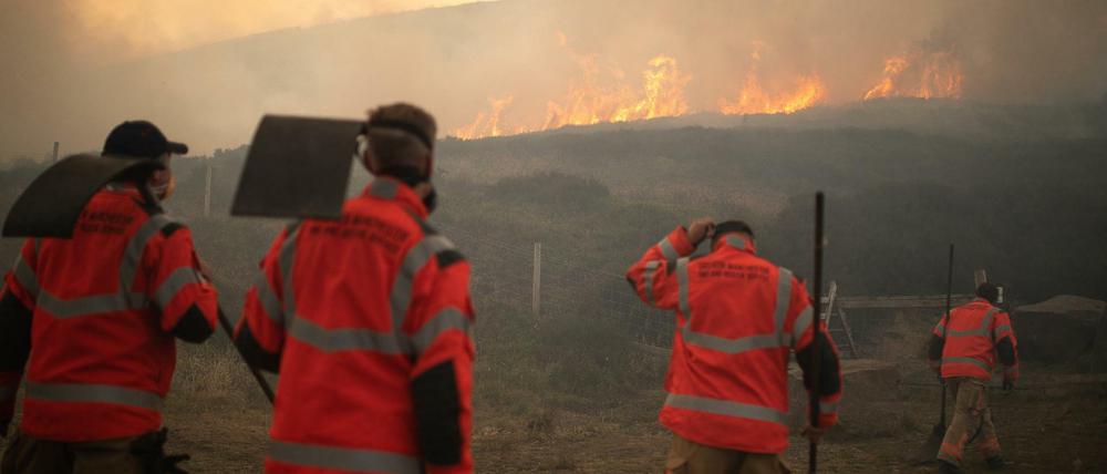 Feuerwehrmänner betrachten Flammen eines Moorbrandes, der sich im Saddleworth Moor und in Richtung der umliegenden Wohngegenden ausbreitet.