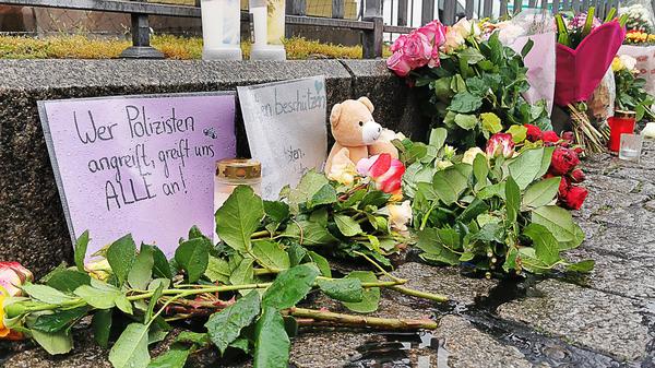 Mannheim: Kerzen und Blumen stehen am Tatort auf dem Marktplatz neben einem Schild „Wer Polizisten angreift, greift uns alle an!“. 