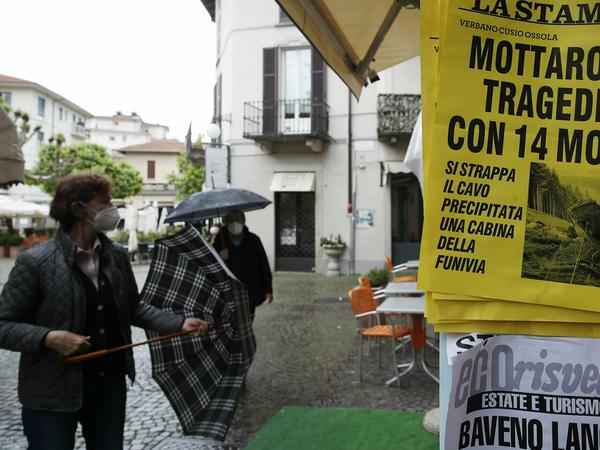 Menschen stehen vor einem Kiosk in Stresa, an dem eine Zeitung mit der Schlagzeile „Mottarone-Tragödie mit 14 Toten“ ausgehängt ist.