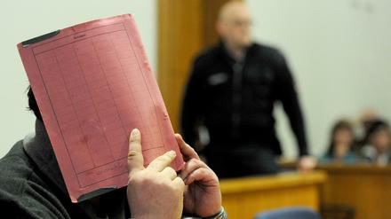  Der ehemalige Krankenpfleger Niels Högel versteckt sein Gesicht hinter einem Aktendeckel, während er auf der Anklagebank des Landgerichts in Oldenburg sitzt.