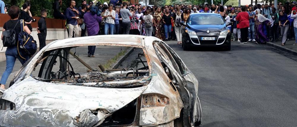 Ein ausgebranntes Auto im französischen Nantes, aufgenommen am 5. Juli. Dahinter laufen Teilnehmer eines Protestmarsches.