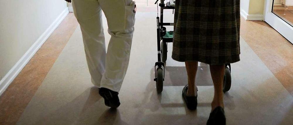 Beine einer Pflegerin und einer alten Frau mit Rollator von hinten auf einem langen Flur