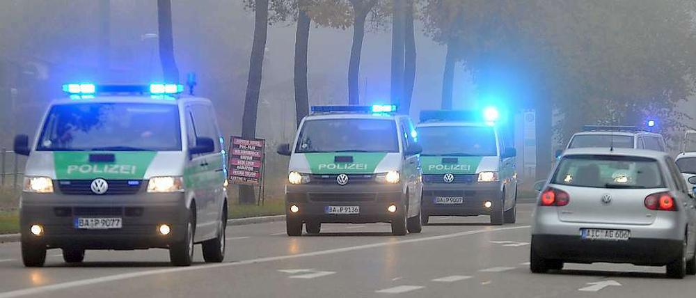 Ein Konvoi aus Polizeifahrzeugen fährt am Freitag mit Blaulicht durch Augsburg. In der Nacht war hier bei einer Schießerei ein Polizist getötet und eine weitere Beamtin verletzt worden. Die Täter flohen in ein großes Waldgebiet, das von der Polizei weiträumig abgesperrt wurde.