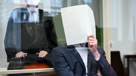  Der Angeklagte sitzt zu Prozessbeginn im Verhandlungssaal im Landgericht München und hält sich einen Bogen Papier vor das Gesicht.