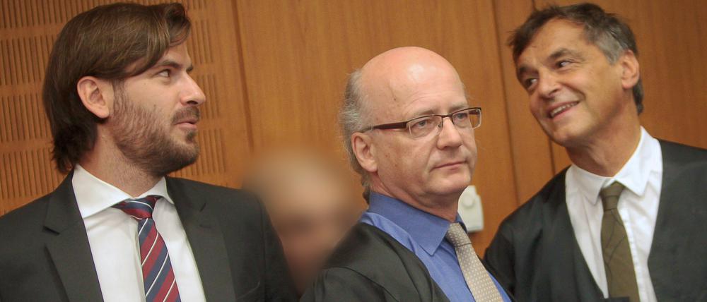 Der Angeklagte (2.v.l.) wird am Freitag im Landgericht in Frankfurt am Main von seinen Anwälten Andreas Groß (M) und Thomas Scherzberg (r) verdeckt. Der Angeklagte soll einen etwas älteren Rocker im April 2014 in Frankfurt mit 34 Schüssen und Schlägen grausam getötet haben. 