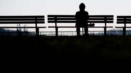 Eine Frau sitzt alleine auf einer Bank in der Sonne.