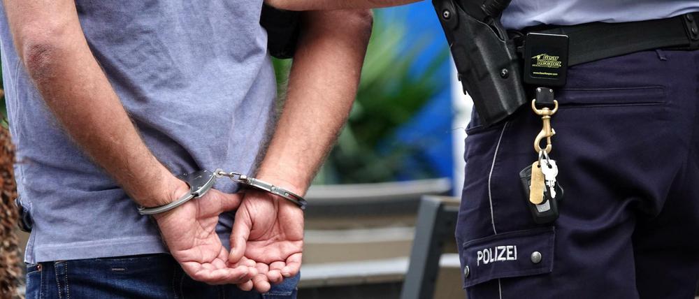Ein Mann steht in Handschellen neben einem Polizisten. (Symbolbild)