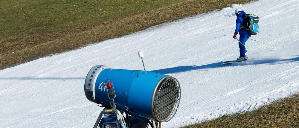 Ein Skifahrer fährt in Garmisch-Partenkirchen (Bayern) am Hausberg auf einem schmalen Kunstschneeteppich an einer Schneekanone vorbei.