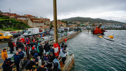 Einwohner der Gemeinde Aldan beobachten einen Einsatz, bei dem zwei Schlepper ein Drogen-U-Boot aus dem Wasser ziehen.