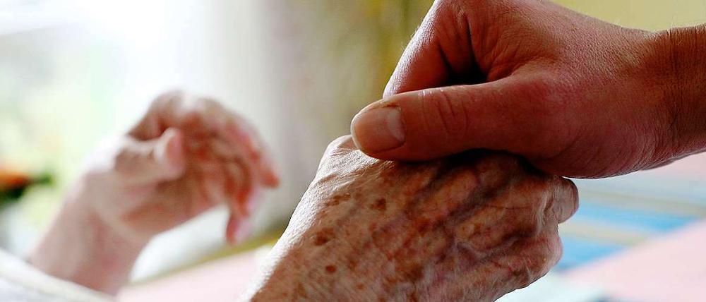 Ein Pfleger hält in einem Altenheim in Düsseldorf die Hand einer Bewohnerin.
