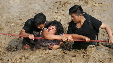 Helfer bringen eine Frau in Huachipa über eine völlig überschwemmte Straße.