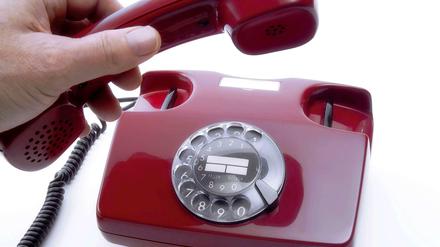 Hand, die an einem alten Wählscheiben-Telefon den Hörer abnimmt.