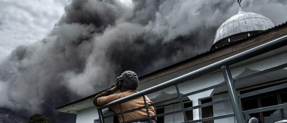 Eine Frau in Indonesien schaut auf die Rauchschwaden des Sinabung. Seit dem Ausbruch des Vulkans auf der Insel Sumatra haben mehr als 10.000 Menschen ihre Häuser verlassen. 