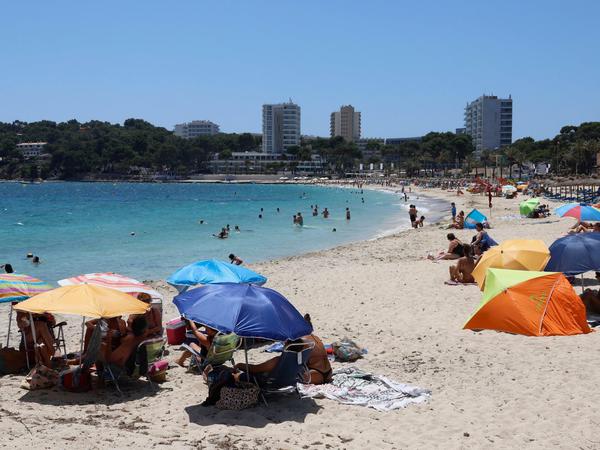Auch so geht Urlaub auf Mallorca: Unter Sonnenschirmen sitzen Menschen am Magaluf Strand und genießen das schöne Wetter. 