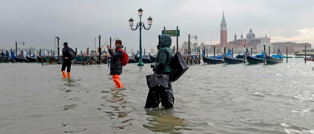 Menschen waten über einen überfluteten Platz in der norditalienischen Stadt. 