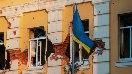 Eine ukrainische Flagge weht vor einem durch Beschuss beschädigten Gebäude.