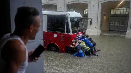 Freiwillige schieben einen Bus, der auf einer durch starke Regenfälle überfluteten Straße stehen geblieben ist.
