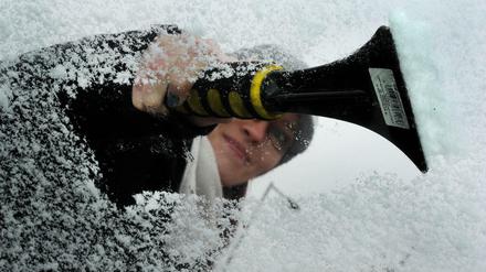 Tipps für eisfreie Autoscheiben: Eine Autofahrerin kratzt Eis von der Windschutzscheibe eines Fahrzeuges.