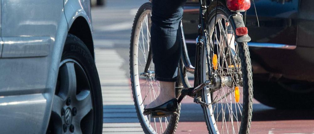 Eine Fahrradfahrerin radelt auf einem Radweg, während Autos rechts abbiegen. 