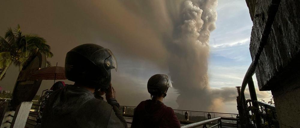 Menschen beobachten auf einer Brücke riesige Rauchwolken.