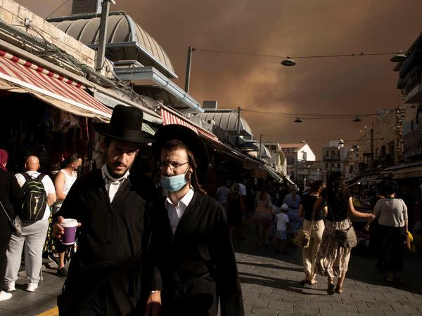 Ultraorthodoxe Juden gehen über den Machane Yehuda-Markt, während der Himmel durch nahe gelegene Waldbrände verdunkelt ist.