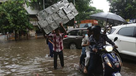 Menschen überqueren eine überschwemmte Straße im indischen Mumbai.