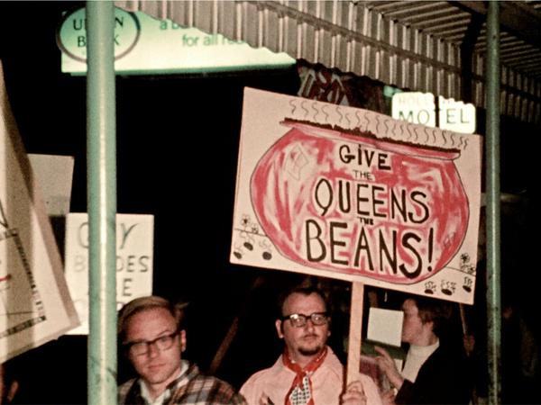 Männer und Frauen halten Protestplakate mit Aufschriften wie "Give the Queens the Beans" hoch.