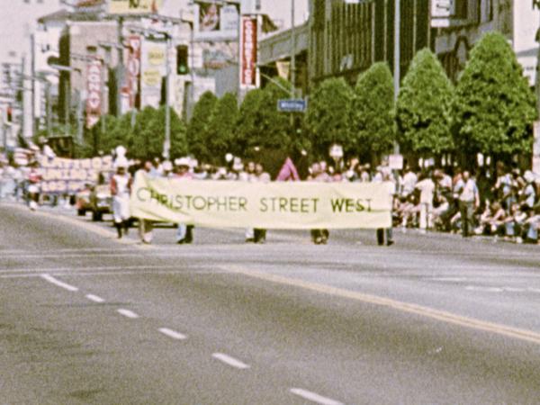 Ein Protestzug mit dem Transparent Christopher Street West zieht über eine große Straße in Los Angeles.